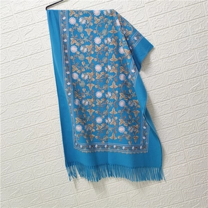 Close-up of blue cashmere-like scarf featuring elegant floral embroidery and tassel fringe