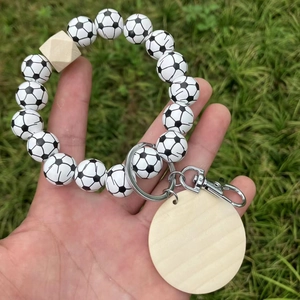 Detail eines Schlüsselanhängers mit Fußballperlen und Holzscheibe vor grünem Rasenhintergrund