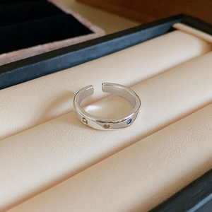 Detail of silver open ring featuring inlaid blue, pink, and yellow gems on polished metal