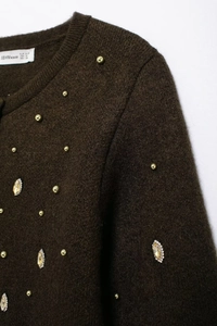 Close-up of brown knit cardigan neck label with elegant rhinestone and gold stud detail