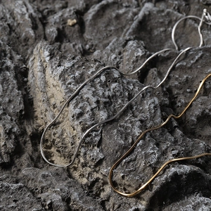 Detail of 18K gold and silver stainless steel snake chain necklaces on natural rock