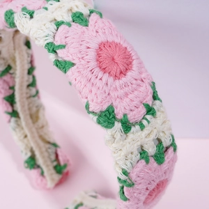 Macro detail of hand-knitted floral headband featuring pink blossoms and green leaves