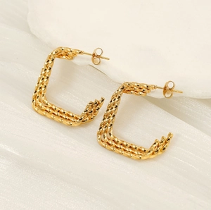 Vue macro de boucles d'oreilles C torsadées dorées avec texture métallique tissée