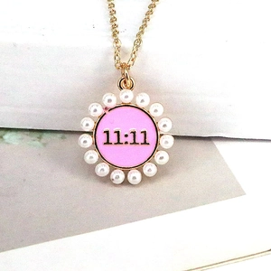 Detail of gold necklace with pink 11:11 pendant and white pearl border on a book