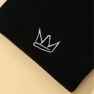 Detail einer schwarzen Strickmütze mit minimalistischer weißer Kronenstickerei