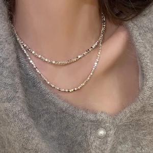 Détail d'un collier multicouche argenté à perles facettées sur pull gris
