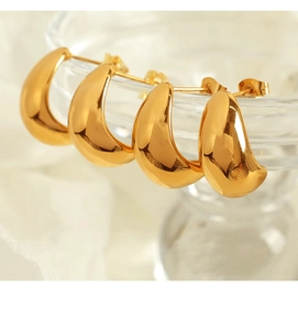 Close-up of chunky gold C-shaped earrings hanging on a glass rim in elegant light