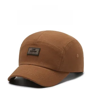 Dettaglio ravvicinato di cappello 5-panel in tela caramello con patch in pelle impressa