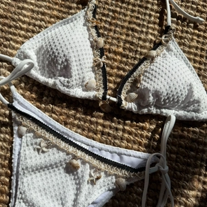Detail of white textured bikini featuring shells and starfish charms on a woven mat