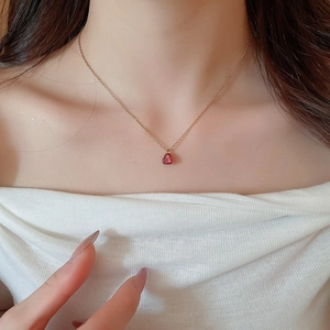 Dettaglio di elegante collana dorata con pendente a goccia rosso rubino su collo