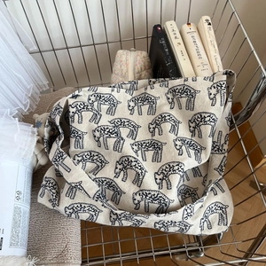 Off-white canvas tote bag with sheep pattern in a metal shopping cart with books