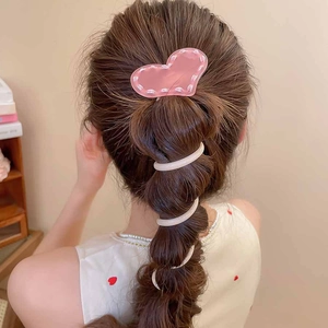 Détail de la pince cœur rose et de l'élastique spirale crème sur une queue de cheval tressée
