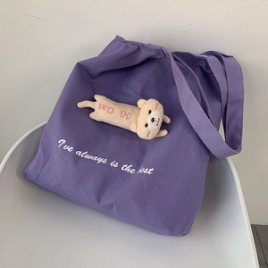 Detail of purple canvas tote bag with 3D teddy bear doll and white printed lettering
