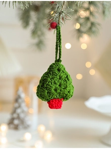 Close-up of handmade crochet Christmas tree ornament with pine branch background