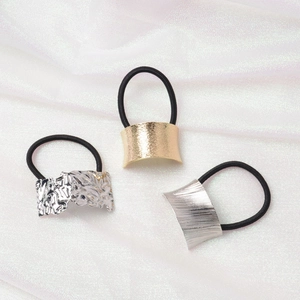 Close-up of three metal hair ties in gold and silver textures on soft silk fabric