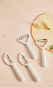 Set of four cream-colored stainless steel fruit and vegetable peelers in a modern kitchen setting
