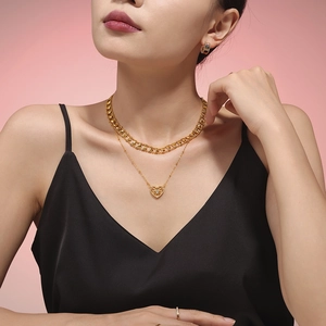 Golden double-layered heart necklace and earrings worn by a model on pink background