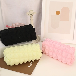 Three popcorn fabric pencil cases in black, yellow, and pink with a soft textured finish