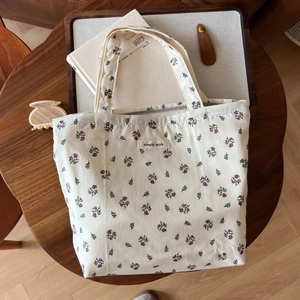 Detail einer floralen Baumwolltasche mit Markenetikett auf einem Holztisch mit Deko