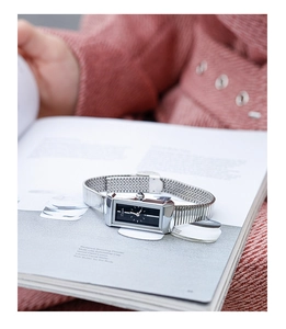 Detail of silver rectangular quartz watch with mesh strap on a magazine background