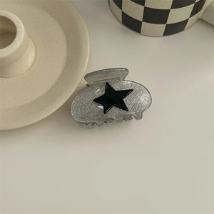 Close-up of Y2K silver metallic hair claw with a black star on a minimalist desk