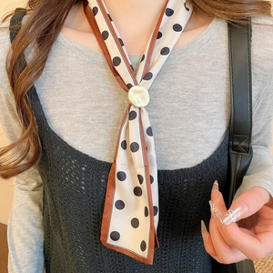 Close-up of a gold metal scarf buckle with a polka dot silk scarf and tassel necklace