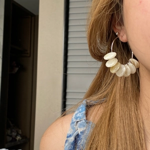 Close-up of oversized hoop earrings with pearlescent shell discs on a model