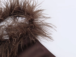 Detailed close-up of soft brown feathers and silky fabric texture on a halter neck dress