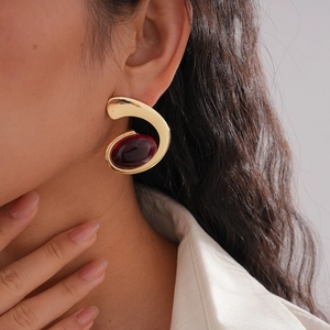 Close-up of gold spiral earrings with dark red oval resin stone worn by a female model