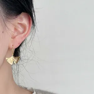 Elegant 14K gold plated ginkgo leaf dangle earrings worn by a model in a close-up shot