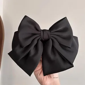 Detailed close-up of a large black satin bow hair clip with multi-layer design