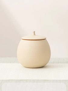 Close-up of minimalist beige ceramic tea canister with matte texture and lid on woven mat