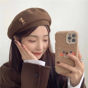Detail view of a brown wool beret featuring a cute 3D stuffed bear doll ornament