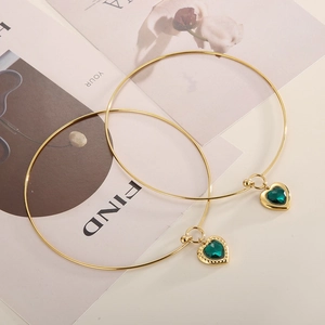 Detail of gold thin bangle featuring a heart-shaped pendant with faceted green stone