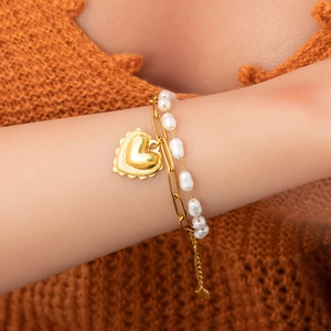 Bracelet double couche plaqué or 18 carats avec cœur et perles sur le poignet d'une femme