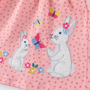 Pink girl's dress with embroidered white rabbits and colorful flowers on polka dot fabric