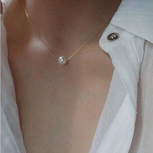Close-up of a single round pearl pendant on a thin gold titanium steel chain necklace