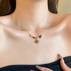 Detailed view of a gold necklace with white beads and a sunflower gemstone pendant