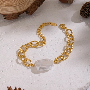 Bracciale a catena dorata in acciaio inossidabile con perla barocca su superficie di pietra