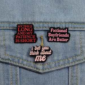 Drei lustige Emaille-Pins mit englischen Sprüchen auf einer blauen Jeansjacke im Detail