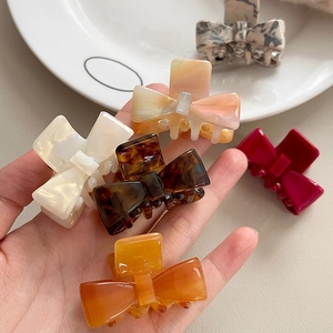 Elegant acetate bow hair claws in various colors displayed on a white ceramic plate