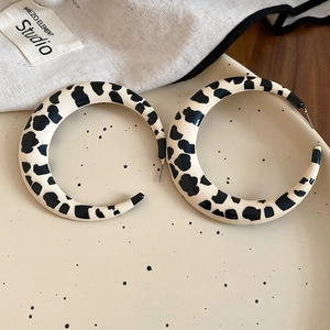 Macro detail of large round acrylic earrings with cow print pattern on a ceramic plate