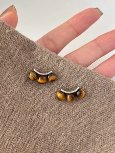 Detailed close-up of tiger eye stone earrings on warm brown knit fabric with silver metal accents