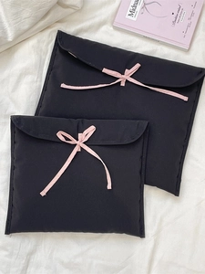Custodia per laptop nera imbottita con fiocchi rosa in due dimensioni su letto bianco