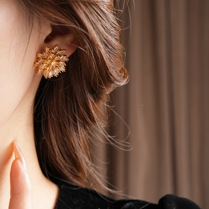 Close-up of a model wearing a gold flower earring with sparkling zircon details