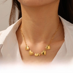 Close-up of a gold-plated necklace with five heart charms worn on a white shirt