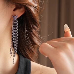 Détail d'un mannequin portant des boucles d'oreilles pampilles à strass violets brillants