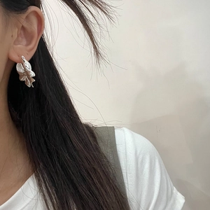 Close-up of silver bow-shaped brass earring worn by a model with a minimalist design