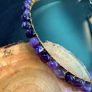 Close-up of handmade purple raw crystal crown with gold wire wrapping detail on wood