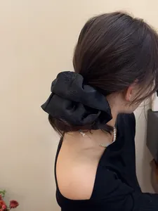 Macro detail of black satin scrunchie with embossed camellia flower worn by a model